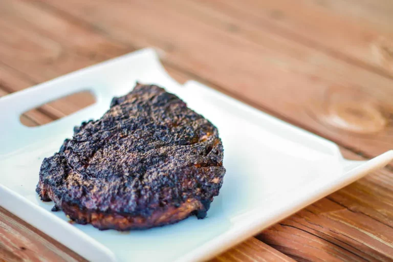 Rich's almost famous ribeye steak with perfectly charcoal-seared bark crust on a white plate, cooked on a Hasty Bake Charcoal Grill