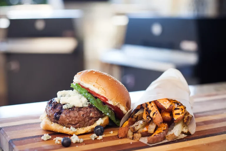 Red White and Bleu-Berry Burger with bleu cheese, blueberries, tomato and lettuce on a wooden board with grilled sweet potato fries, grilled on a Hasty Bake Charcoal Grill