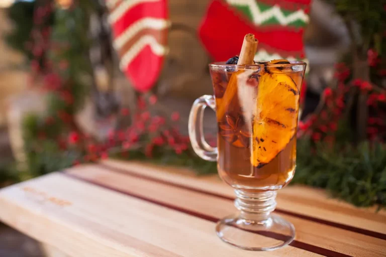 Bourbon spiced apple cider cocktail with orange slice and cinnamon stick with holiday decorations, made on a Hasty Bake Charcoal Grill