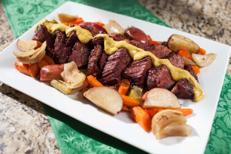 Twice grilled Guinness corned beef with roasted vegetables and mustard horseradish sauce on a white plate, made on a Hasty Bake Charcoal Grill