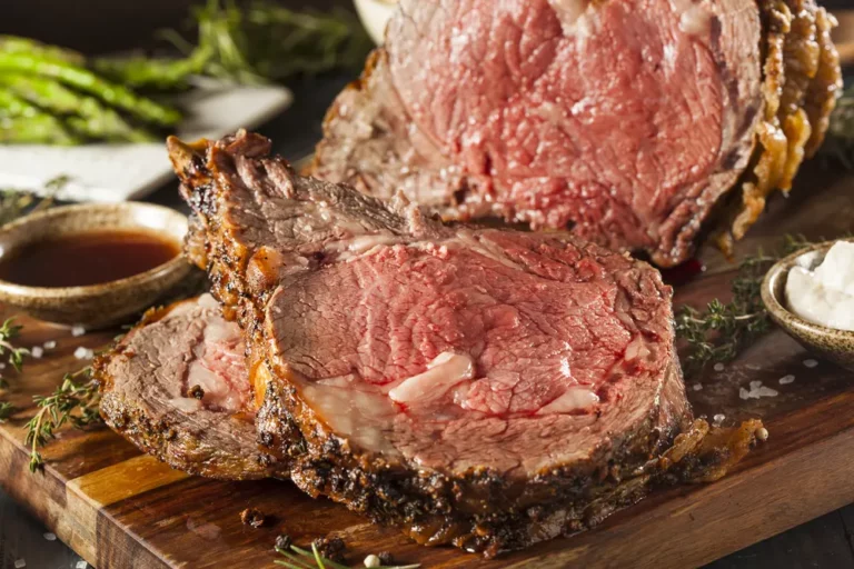 Reverse-seared prime rib roast sliced on a cutting board with herbs and sauces, cooked on a Hasty Bake Charcoal Grill