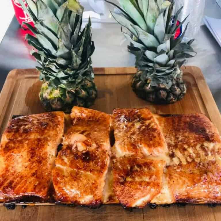 Pineapple plank halibut fillets on a cutting board with fresh pineapples, cooked on a Hasty Bake Charcoal Grill