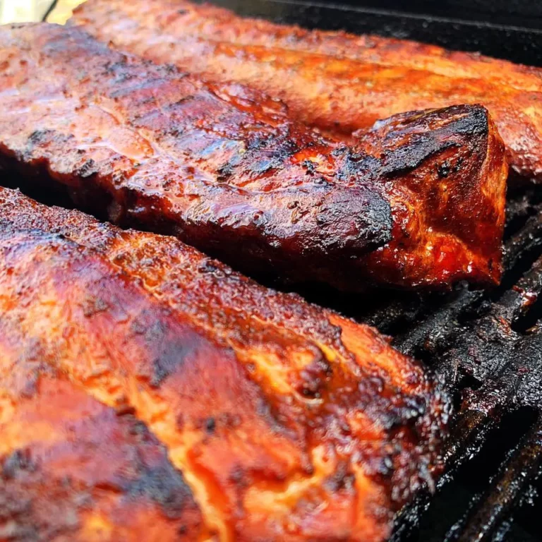 Close-up of smoked baby back ribs with dark bark crust on the grill grates of a Hasty Bake Charcoal Grill