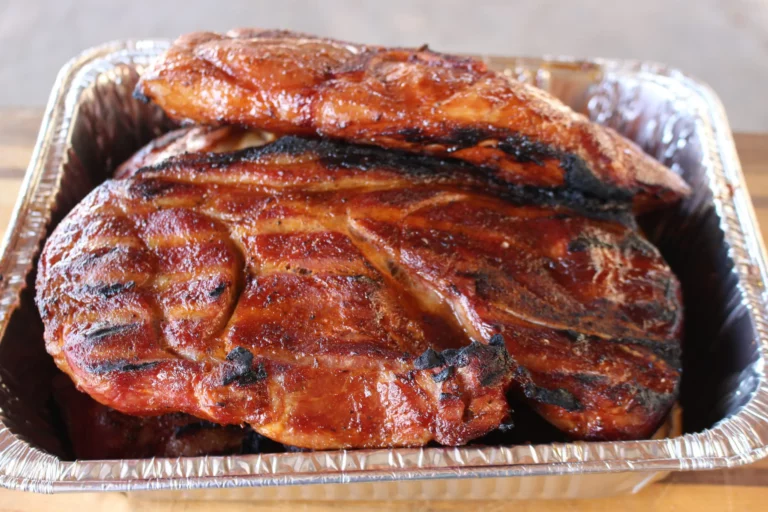 Pork steaks with caramelized glaze in an aluminum pan, cooked on a Hasty Bake Charcoal Grill