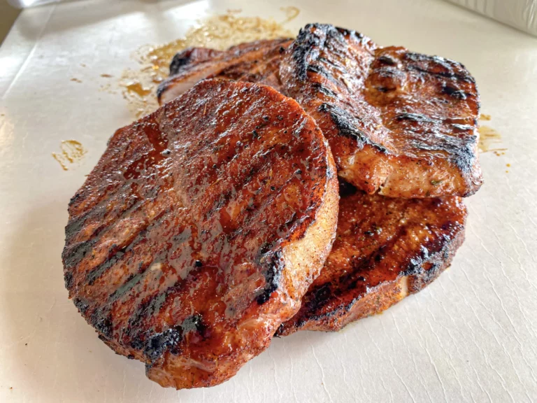 Maple bourbon glazed pork chops with beautiful char marks on a foil-lined tray, grilled on a Hasty Bake Charcoal Grill