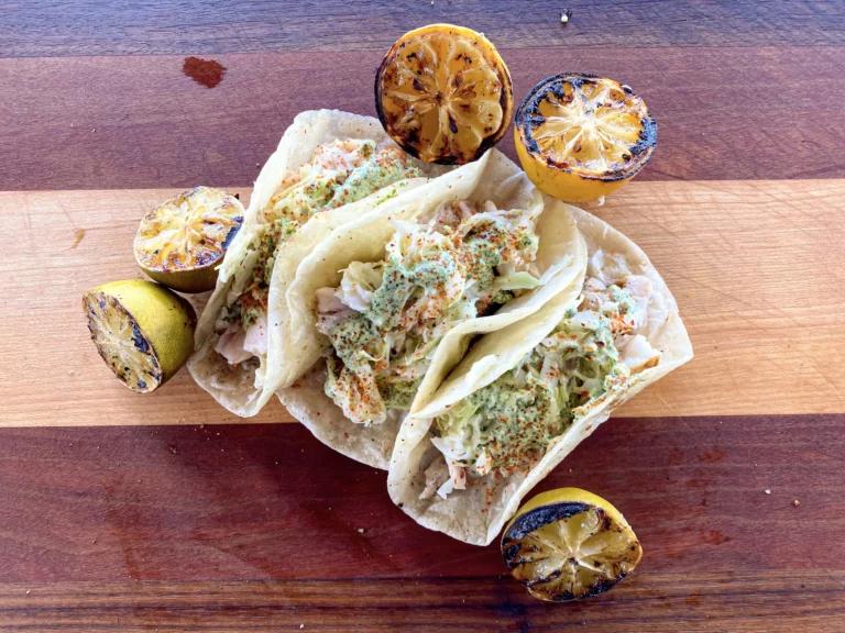 Jalapeño lime fish tacos with slaw and grilled lemon halves on a wooden board, made on a Hasty Bake Charcoal Grill