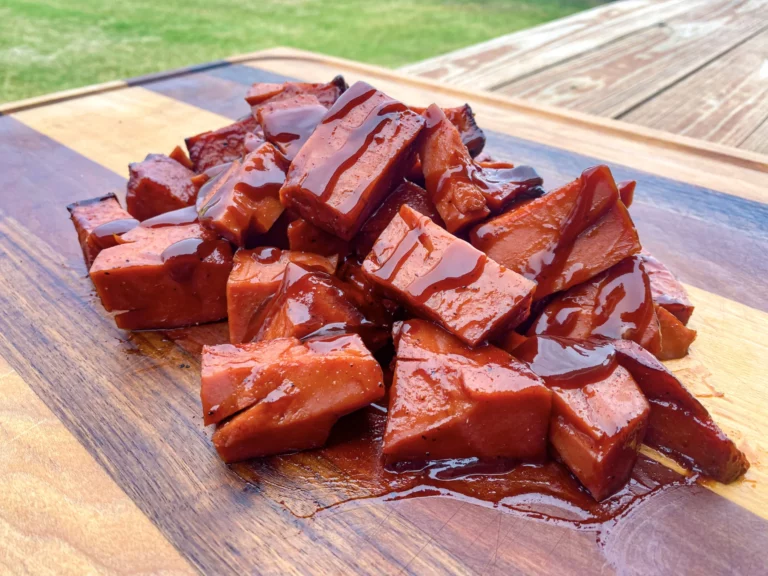 Smoked bologna burnt ends glazed with BBQ sauce on a wooden cutting board, made on a Hasty Bake Charcoal Grill