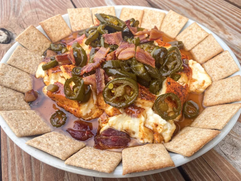 Smoked pepper cream cheese dip topped with jalapeños and bacon on a plate with crackers, made on a Hasty Bake Charcoal Grill