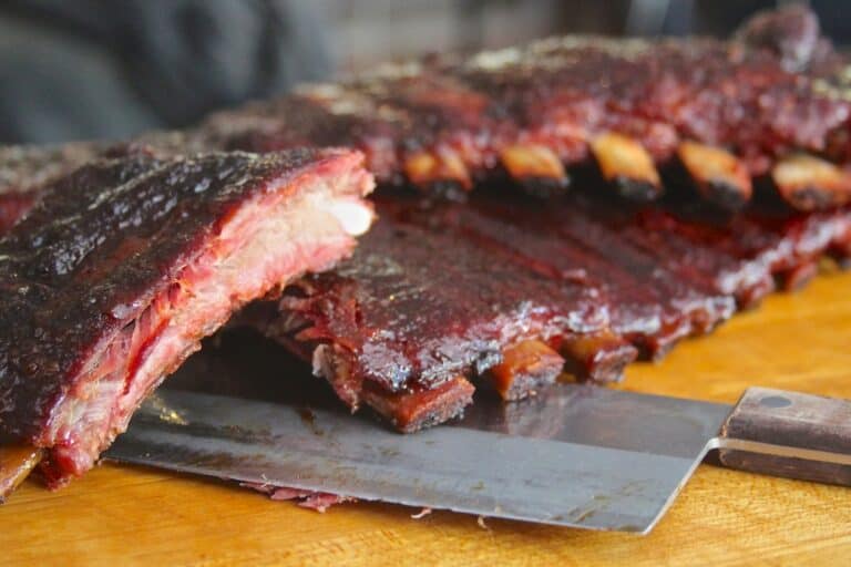 Maple chipotle glazed spareribs being carved on a cutting board with a knife, showing the bark crust, cooked on a Hasty Bake Charcoal Grill