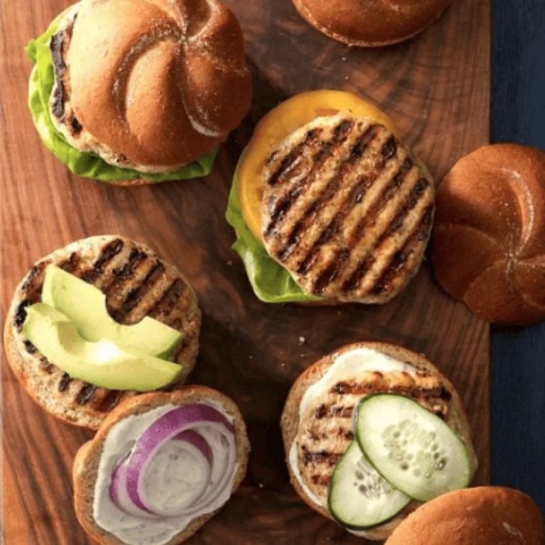 Overhead view of grilled chicken ranch burgers open-faced on buns with avocado, red onion, cucumber and cheese toppings, grilled on a Hasty Bake Charcoal Grill
