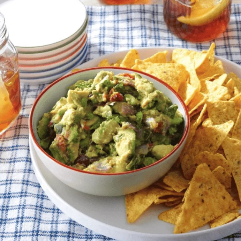 Fresh grilled guacamole in a bowl surrounded by tortilla chips with iced drinks in the background, made on a Hasty Bake Charcoal Grill