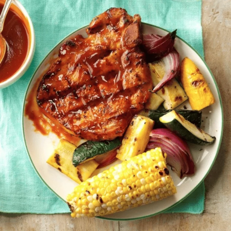 Glazed grilled pork chop on a plate with grilled corn, zucchini, red onion and yellow squash with homemade BBQ sauce, cooked on a Hasty Bake Charcoal Grill